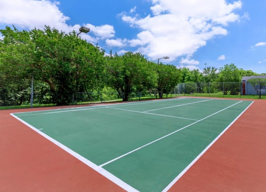 a tennis court with trees and a blue sky with clouds