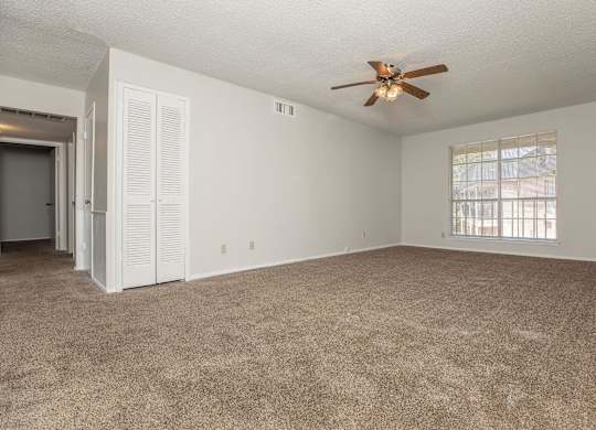an empty living room with a ceiling fan and a window