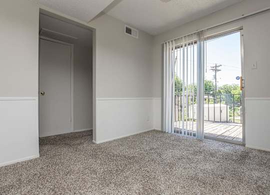 an empty living room with a sliding glass door to a balcony