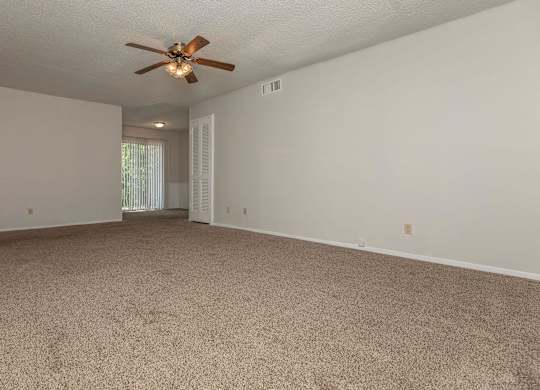 a spacious living room with carpet and a ceiling fan