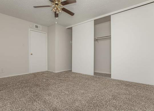 an empty living room with a ceiling fan and closet