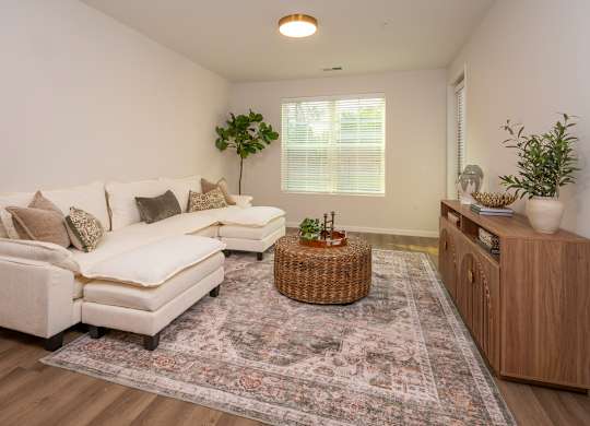 A living room with a white couch, a wicker table, and a rug on the floor.