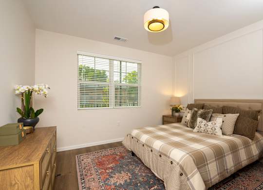 A bedroom with a bed, nightstand, and window with blinds.
