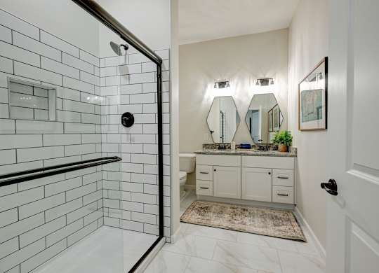 A bathroom with a white tiled shower and a vanity with a mirror above it.
