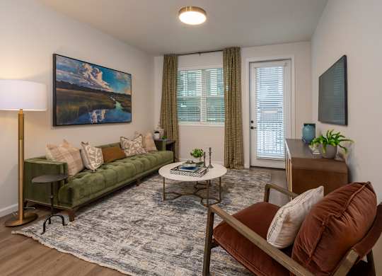 A living room with a green couch, a painting on the wall, and a lamp on a stand.