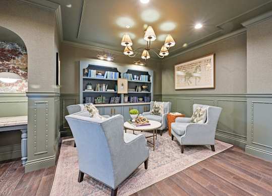 A living room with a grey sofa, a grey armchair, a coffee table, a bookshelf, and a chandelier.