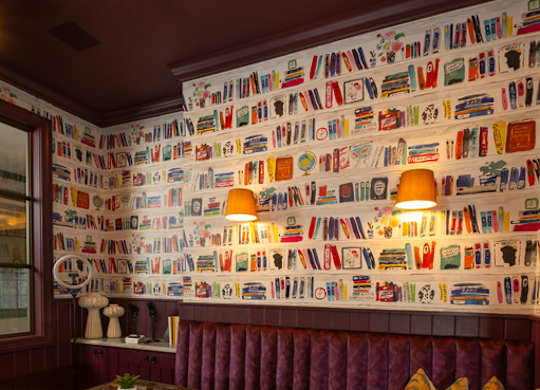 A room with a wall covered in books and a table with a plant on it.