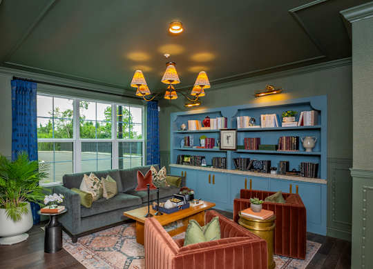 A living room with a grey couch, a red armchair, a wooden coffee table, and a bookshelf with books and decorative items.