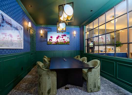 A room with a table and chairs and a painting of a building.