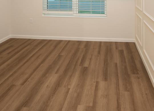 A room with a window covered by white blinds and wooden flooring.