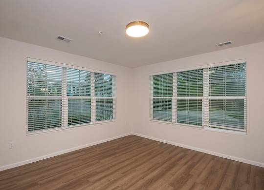 A room with wooden floors and two windows with blinds.
