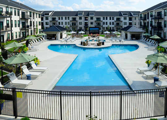 A large swimming pool surrounded by lounge chairs and umbrellas in a resort-like setting.