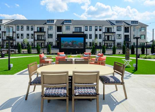 A table with chairs is set up in front of a building with a screen on it.