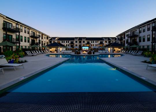 A large swimming pool in the middle of a resort surrounded by lounge chairs.