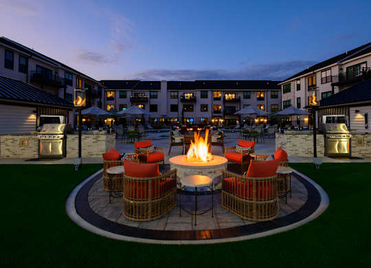 A fire pit in the middle of a grassy area surrounded by chairs.