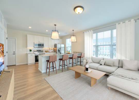 A well-lit, modern living room with a kitchen in the background.