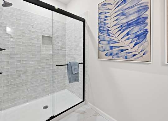 A bathroom with a glass shower door and a blue and white painting on the wall.