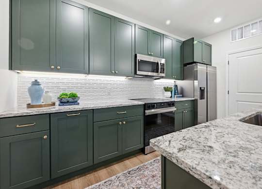 A kitchen with green cabinets and a marble countertop.