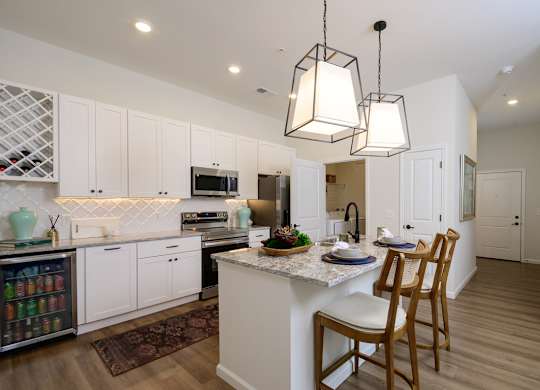 A kitchen with white cabinets and a central island with a marble top.