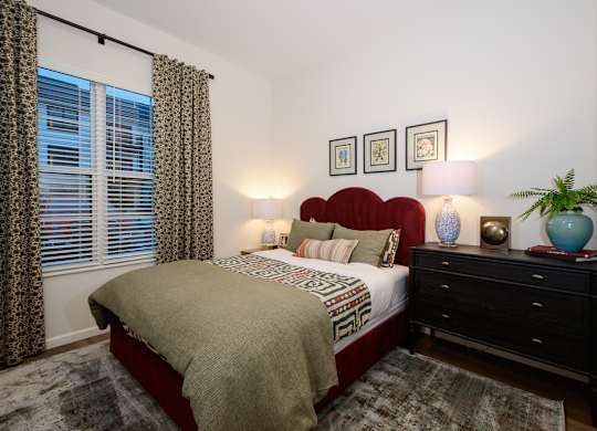 A bedroom with a bed, nightstand, and a window with curtains.