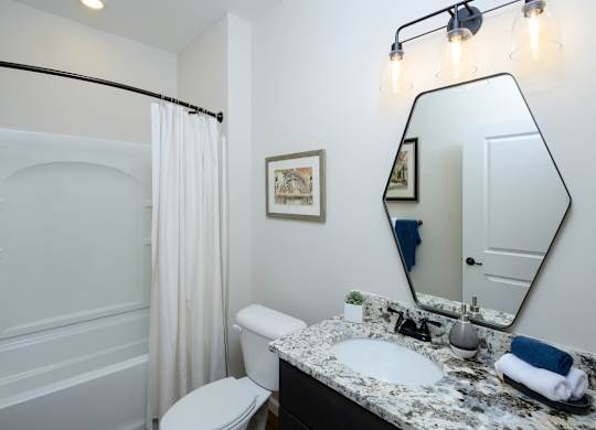 A bathroom with a white toilet, a sink, a mirror, and a shower. at Fairmont Apartments, Westerville