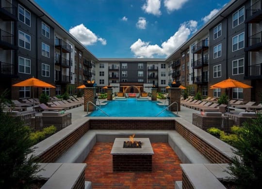 an outdoor pool with a firepit and lounge chairs in front of an apartment building