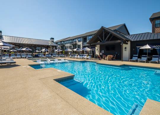 A large outdoor swimming pool with a patio area and lounge chairs.