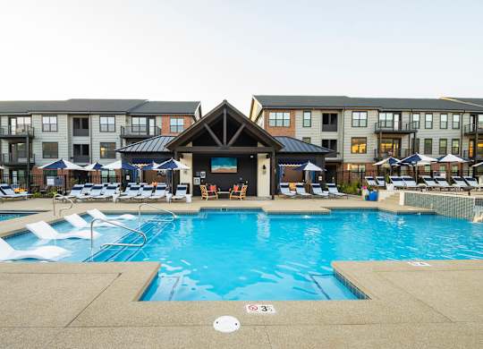 A large swimming pool with a deck and sun loungers in front of apartment buildings.