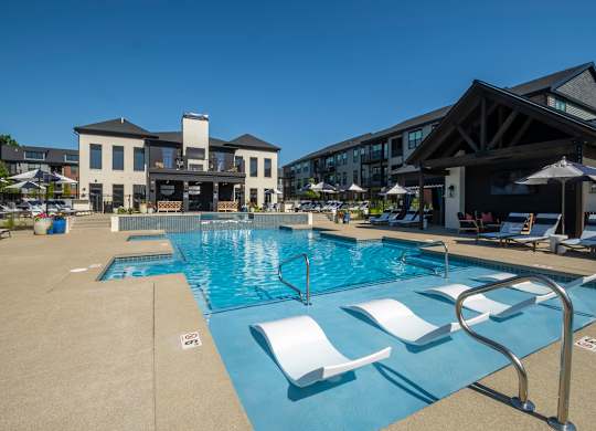 A large swimming pool with white lounge chairs and a building in the background.