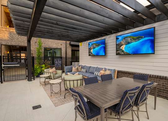 A patio with a table, chairs, and two TVs mounted on the wall.