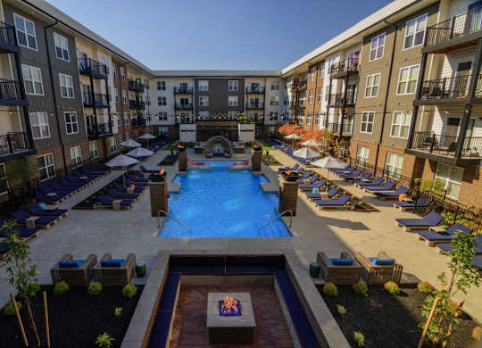 A large swimming pool surrounded by lounge chairs and umbrellas in a courtyard surrounded by apartment buildings.