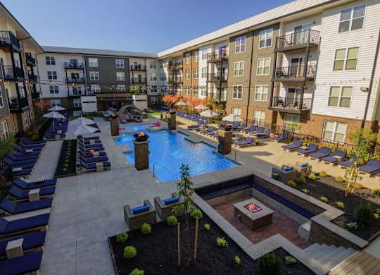 A large outdoor pool area with lounge chairs and a hot tub surrounded by apartment buildings.