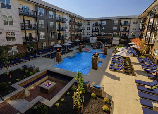 A large outdoor pool area with lounge chairs and a fire pit surrounded by apartment buildings.