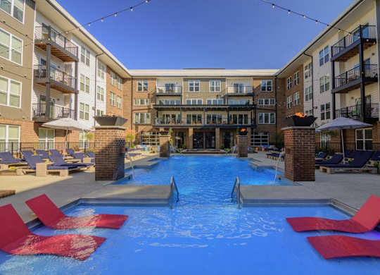 A swimming pool surrounded by red lounge chairs in front of apartment buildings.