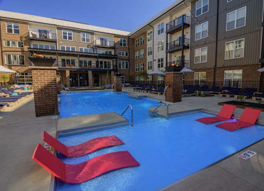 A pool with red chairs and a building in the background.