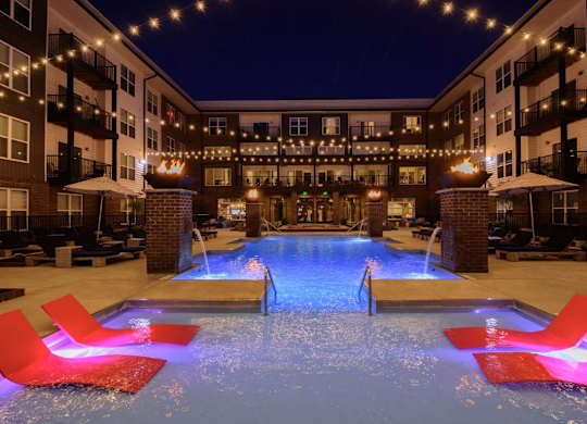 A pool with red chairs and lights around it.