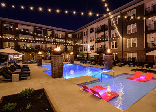 A pool area with a lit up water feature and lounge chairs.