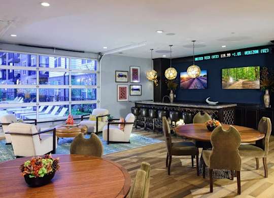 A living room with a wooden table and chairs, a sofa, and a television displaying a forest scene.