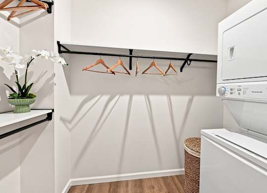 A white washing machine in a laundry room with a white wall and a white shelf.