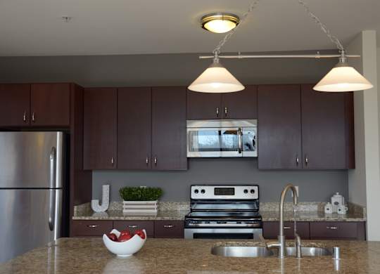 A kitchen with brown cabinets and a granite countertop at Cornerstone & Ravenna* Apartments, Shorewood, WI, 53211