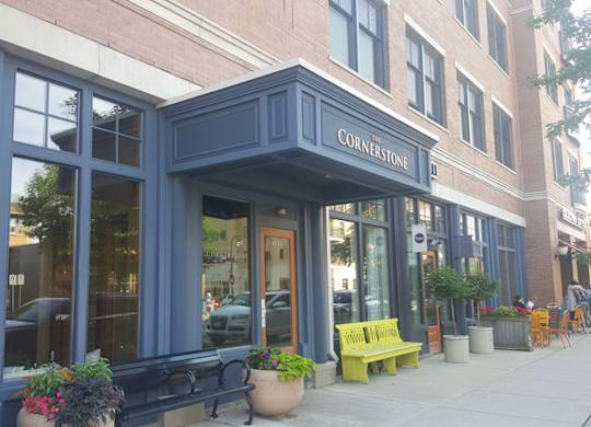 A storefront with a blue awning and a yellow bench in front at Cornerstone & Ravenna* Apartments, Shorewood 53211