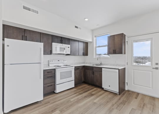 an empty kitchen with white appliances and wooden floors