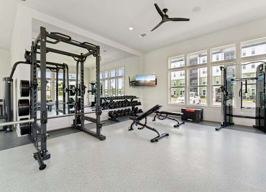 A spacious gym with a variety of equipment including a squat rack, bench, and weights at The Hendry Apartments, Fort Myers, FL
