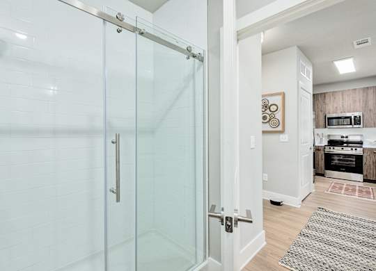 A glass shower door in a white bathroom at The Ashton at East Park Apartments, Kennesaw, 30144