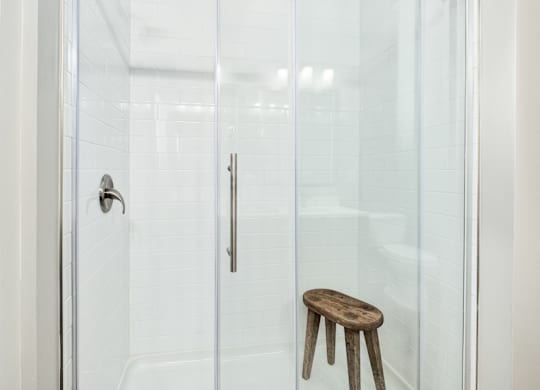 A wooden stool is in front of a glass shower door at The Ashton at East Park Apartments, Georgia, 30144