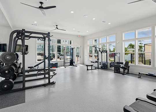 A spacious gym with a variety of equipment and a view of the outdoors through large windows at The Hendry Apartments, Florida