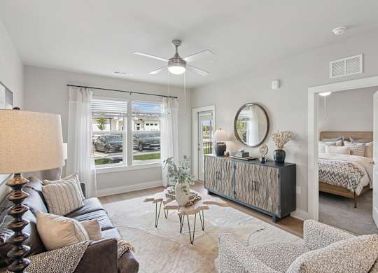 A well-lit, spacious living room with a large window, a sofa, a side table, and a bed in the background at The Hendry Apartments, Fort Myers, 33905