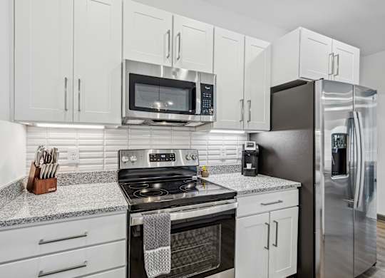 a white kitchen with stainless steel appliances and white cabinets at The Leo Myrtle Beach, Myrtle Beach, SC, 29579