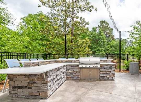 A stone barbecue area with a grill and chairs.