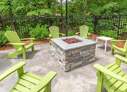A fire pit surrounded by green chairs in a backyard.